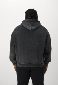 Juodas per didelis džemperis su tekstūru ir su virvele reguliuojamu gaubtu. Turi laisvą siluetą ir sutrauktus rankogalius bei apačią.