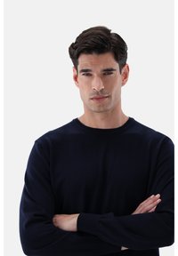 Marineblauer gestrickter Pullover mit Rundhalsausschnitt und langen Ärmeln, der eine glatte Textur und dezente Rippdetails an den Bündchen und am Saum aufweist.