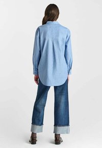Blue striped shirt with a back pleat and long sleeves, paired with wide-leg denim jeans featuring rolled cuffs. Brown shoes complete the look.