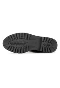 Semelle de chaussure en caoutchouc noir présentant une texture antidérapante avec des motifs variés, y compris des rainures et des formes surélevées pour une meilleure adhérence.