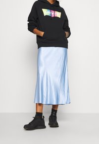Felpa nera con logo colorato di Levi's, abbinata a una gonna midi in satin azzurro chiaro. Sneakers nere e calze completano l'outfit.