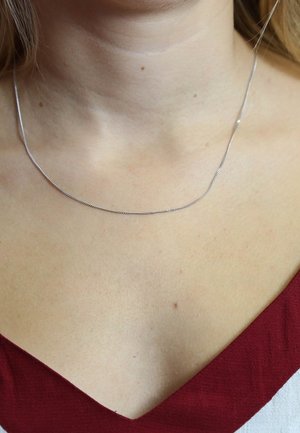 Zilveren ketting met een glad, dun ontwerp, rust op de huid. De ketting heeft een subtiele glans en minimale details.