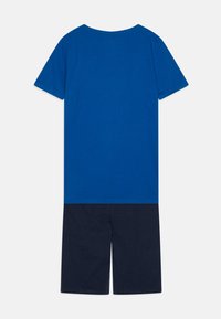 T-shirt bleu à manches courtes en coton doux avec un col rond, associé à un short marine foncé, les deux ayant un design uni et une coupe décontractée.