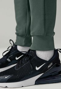 Nike Air Max 270 sneakers in black with white accents, paired with textured green joggers featuring ribbed cuffs.