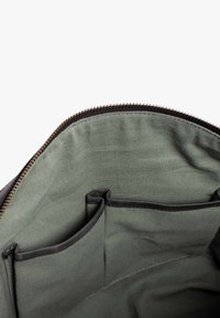 Der Innenraum einer schwarzen Tasche mit einer grünen Stoffauskleidung. Sie verfügt über zwei offene Taschen auf einer Seite und einen runden Reißverschluss um den oberen Rand.