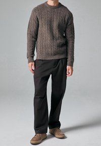 Maglione marrone a maglia grossa con colletto a costine, abbinato a pantaloni neri larghi e scarpe marroni slip-on. Design semplice e strutturato.