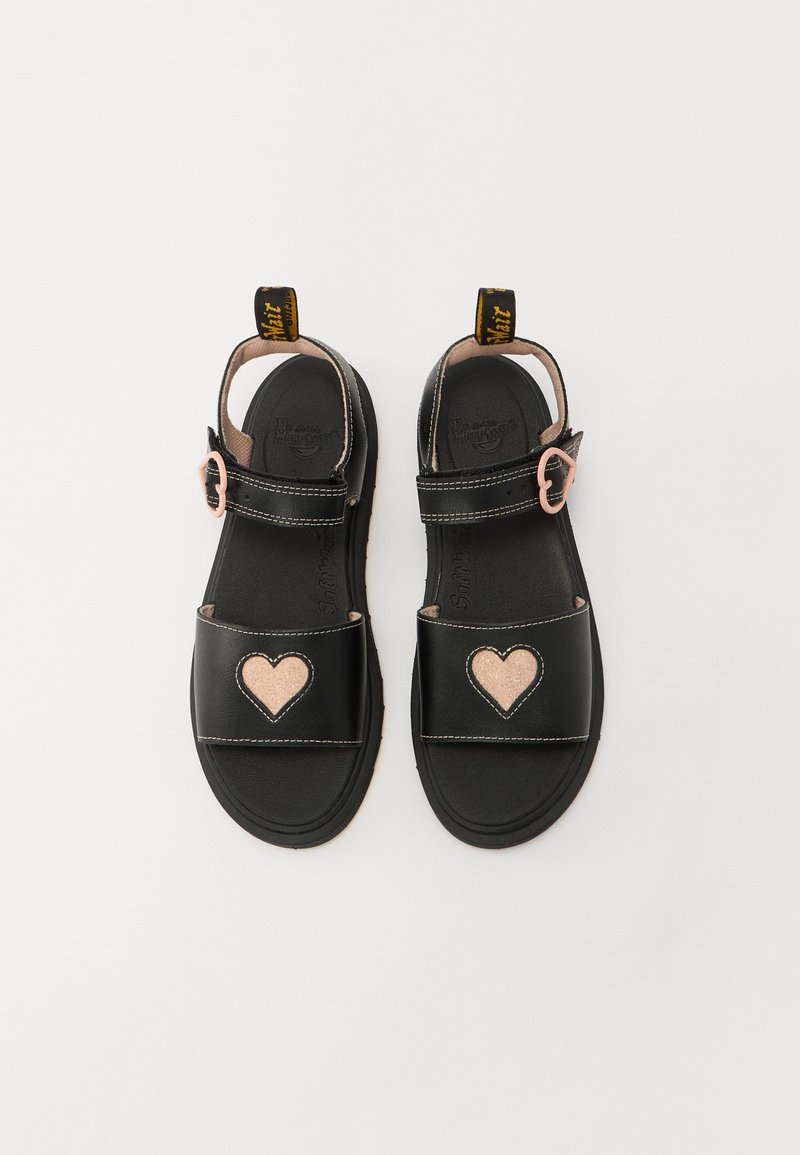 Sandales noires avec des accents en forme de cœur rose, sangle réglable, semelle texturée, doublure douce et languette de tirage jaune portant la marque au talon.