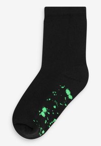 Chaussette en coton noir avec un bord côtelé, présentant un motif texturé de taches vert vif près du orteil et de la zone du milieu du pied.