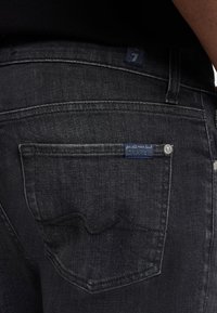 Mörka denimjeans med en bakficka som har en synlig märkesskylt och ett distinkt sömnadsmönster, accentuerad med en silvernitet.