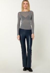 Gray long-sleeve fitted top with sheer material and scoop neckline, paired with fitted navy faux leather pants featuring flared legs.
