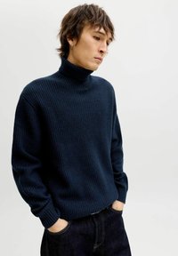 Marineblauer, gerippter Rollkragenpullover mit langen Ärmeln und lockerer Passform, kombiniert mit dunklen Jeans. Der Pullover besteht aus strukturiertem Stoff für Wärme.