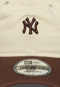 Ρυθμιζόμενο καπέλο σε κρεμ και καφέ, με κεντημένο καφέ λογότυπο NY. Διαθέτει στρογγυλή ετικέτα New Era 9TWENTY στη καφέ γείσο.