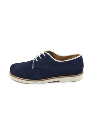 Zapato oxford de ante azul marino con cordones y ribete blancos, forro interior marrón claro y suela blanca con pespuntes en color canela.