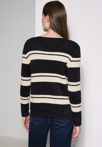 Pull noir et crème à rayures, à la coupe décontractée, en texture douce, avec des manches longues et des poignets côtelés, porté sur un jean noir.