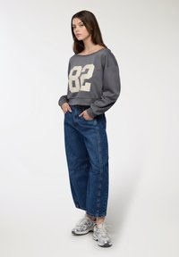 Szara, krótka bluza z dużym kremowym nadrukiem "82". W parze z luźnymi niebieskimi dżinsami i srebrnymi trampkami.