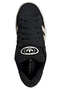 Baskets en daim noir avec des lacets texturés, trois bandes beige, et un logo rond sur une languette noire. Semelle intérieure douce visible à l'intérieur.