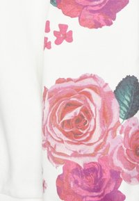 Tessuto bianco con un motivo floreale colorato con grandi rose rosa e foglie verdi, che mostra trame dettagliate e motivi vivaci.