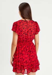 Abito rosso a fiori con maniche a palloncino corte, vita elastica e orlo a strati con rouches. Tessuto trasparente con motivi di fiori neri.