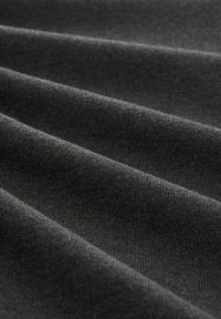 Tumši pelēks audums ar teksturētu, ribotā virsma; vairākas krokas rada dziļumu un variācijas gaismā un ēnā.