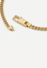 Goldkettchenarmband mit einer strukturierten, gravierten Schliesse und spitzen Enden. Beinhaltet den Markennamen "GUESS" auf der Schliesse und den Enden.