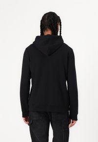 Black cotton hoodie with a large hood, long sleeves, ribbed cuffs, and a relaxed fit. The back is plain without any logos or embellishments.