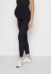 Maternity black leggings made of stretchy fabric, fitted design, full-length, paired with white sneakers and light-colored ribbed socks.
