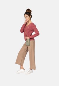 Lyserød ribbet cardigan med V-hals, beige brede bukser og hvide sneakers med guld detaljer. Tilbehøret inkluderer en grøn skuldertaske.