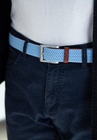 Cintura intrecciata blu imbottita con fibbia in metallo argentato e un accento in pelle marrone, indossata sopra pantaloni in tessuto scuro.