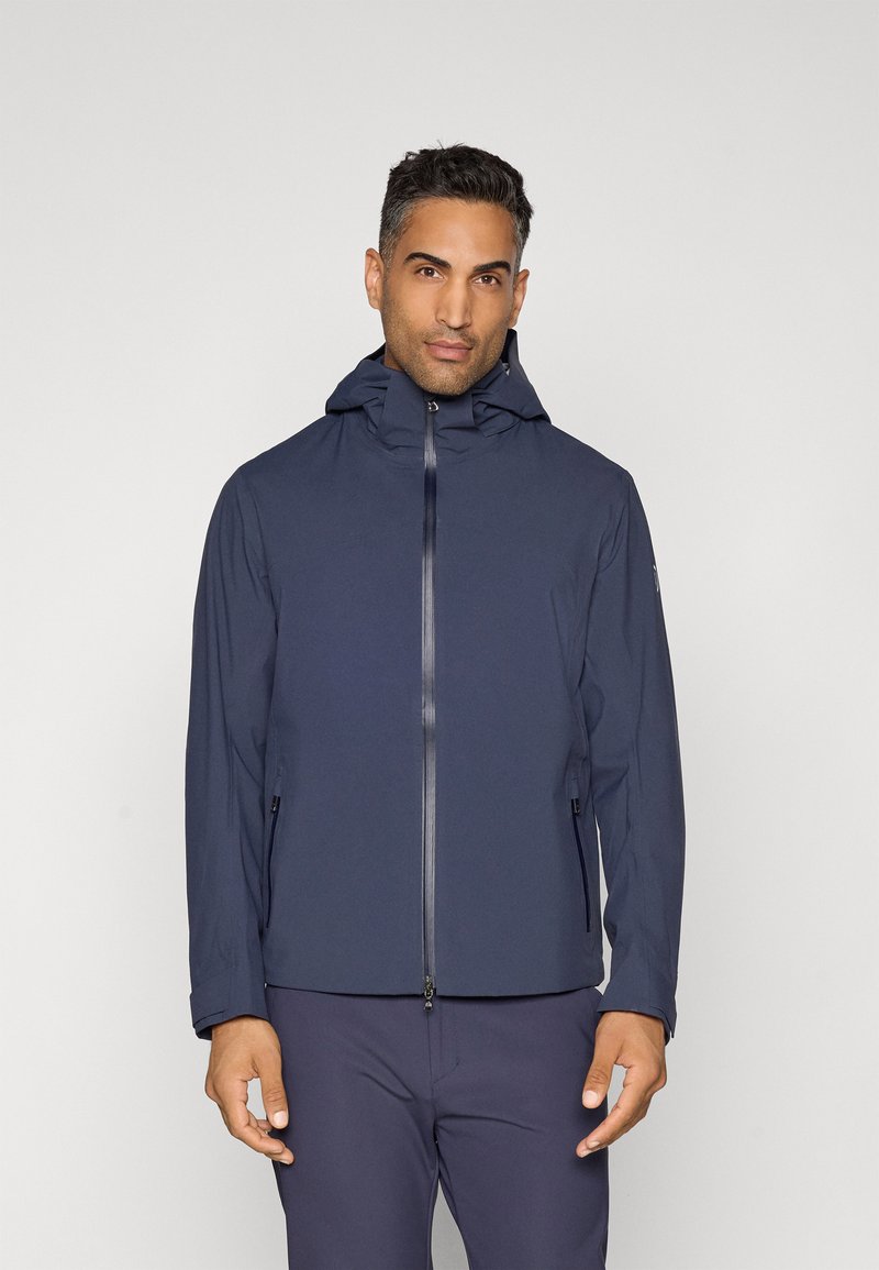 Navy blue waterproof jacket with a hood, front zipper, and side pockets. Smooth texture and minimal design with a fitted silhouette.