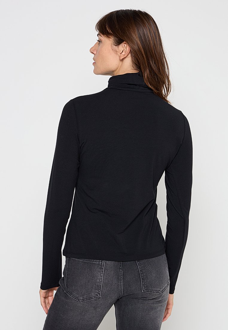 Schwarz langärmliges Rollkragenshirt aus glattem, dehnbarem Stoff. Figurbetonter Schnitt mit hohem Kragen und minimalen Details, getragen mit grauen Jeans.