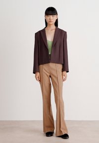 Blazer corto marrón, top verde, pantalones acampanados color beige, zapatos negros. Tela suave, diseño estructurado, estilo minimalista sin patrones visibles.