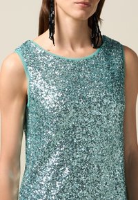 Paillettetopp i turkos med en smidig textur och rundad halsringning. Har tunna axelremmar och en glittrande yta med reflekterande accenter.
