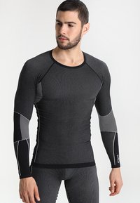 Maglia sportiva a maniche lunghe di colore grigio scuro, con un design aderente, tessuto texturizzato, dettagli neri e motivi decorativi sulle maniche.