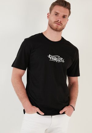 Sort bomulds t-shirt med et hvidt logo i graffiti-stil på forsiden. Korte ærmer og rund hals-design. Flad tekstur.