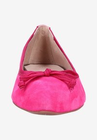 Chaussure plate en daim rose avec un bout arrondi et un nœud en ruban ton sur ton. L'intérieur est en cuir beige, avec une texture lisse et douce.