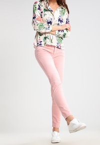 Halenka s květinovým potiskem a zelenými a fialovými akcenty, kombinovaná se světle růžovými upnutými kalhotami a bílými teniskami, vytvářející ležérní outfit.