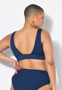 Námořnická modrá texturovaná bikiny podprsenka s širokými ramínky a hlubokým V-zadním výstřihem, v kombinaci s odpovídajícími bikinami s vysokým pasem.