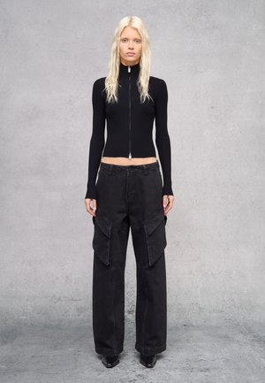 Top lungo a maniche lunghe nero a coste con zip abbinato a pantaloni cargo neri a gamba larga con tasche laterali e una consistenza liscia. Scarpe col tacco nere.