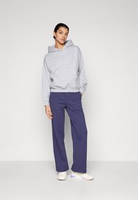 Felpa grigia con vestibilità comoda e cappuccio regolabile, abbinata a pantaloni a gamba larga blu navy. Le calzature comprendono sneakers crema con dettagli viola.