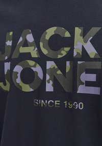 Tricou din bumbac bleu marin, cu text mare "JACK JONES" în nuanțe de verde camouflage și gri, având "SINCE 1990" în alb dedesubt.