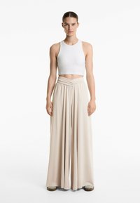 Weißes, geripptes Croptop kombiniert mit weiten, beigen Hosen, die ein gewickeltes Taillendesign und fließenden Stoff aufweisen.