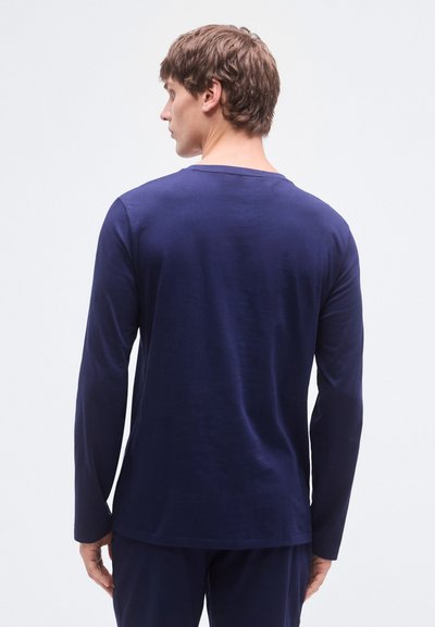 Camisa azul-marinho de manga comprida, gola redonda, tecido macio, corte descontraído, textura suave, detalhes mínimos de costura. Usada com calças combinando.