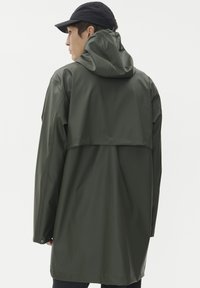 Olivgrön vattentät jacka med huva, med en avslappnad passform och längre bakstycke, tillverkad av ett mjukt, glänsande material.