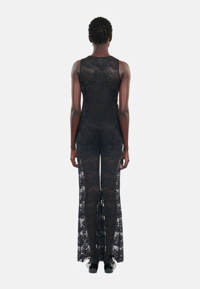 Svart blonde jumpsuit med tett bodice og flagrende ben, med intrikate blomster mønstre og semi-transparent tekstur.