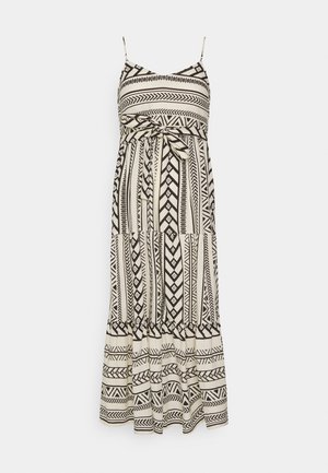 Mouwloze maxi-jurk met zwart-witte geometrische patronen, dunne bandjes en een gestrikte tailleband op een witte achtergrond.