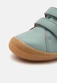 Light blue leather shoe with a rounded toe, tan rubber sole, and two adjustable Velcro straps across the upper for a secure fit.