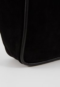 Svart mocka handväska med släta läderkanter. Har en rundad botten och subtil textur som betonar en minimalistisk design.