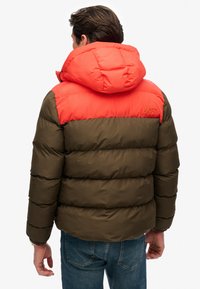 Puffer jacket featuring an orange upper section and olive green lower section, with a hood, stitched detailing, and "SUPERDRY" logo on back.