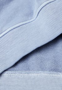 Svetle modrý svetr s manžetami a lemem z žebrovaného materiálu, s texturovaným pleteným vzorem viditelným pod ohnutým okrajem.