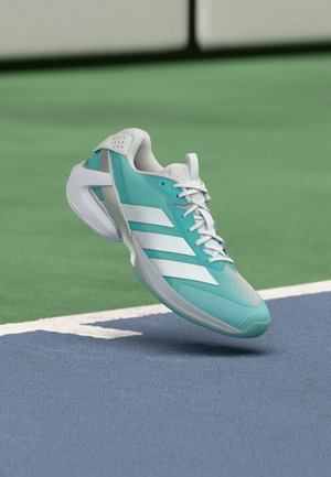 Turkusowy but sportowy z białymi akcentami, górna część wykonana z teksturowanej siateczki, poduszka w podeszwie, zaokrąglony nosek i trzy białe paski po boku.